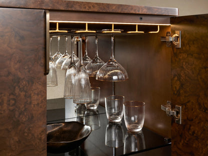 Morley Bar Cabinet with one door open. Inside are hanging glasses and bottles on dark wood shelves, showcasing a stylish design.