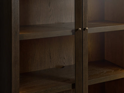 Dark mocha Nason Modular Glass Cabinet. Tall wood cabinet with two glass top doors and two solid bottom doors, aged nickel handles.