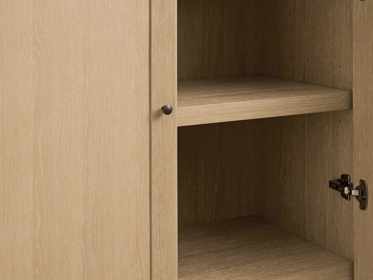 Close-up of Nason Modular Hutch Cabinet in sand white oak, door slightly open revealing interior shelf & aged nickel knob/hinge.