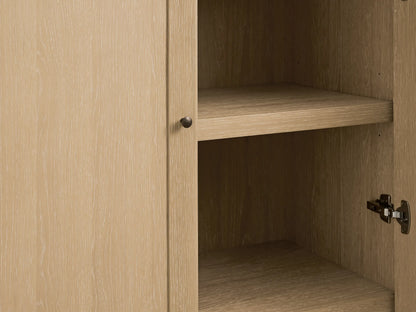 Close-up of Nason Modular Hutch Cabinet in sand white oak, door slightly open revealing interior shelf & aged nickel knob/hinge.