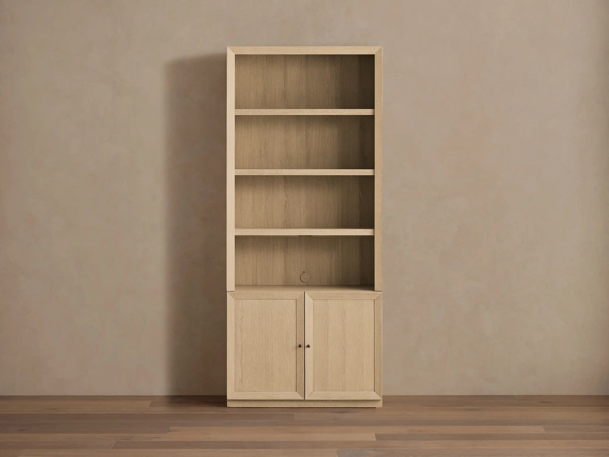 Nason Modular Hutch Cabinet in sand finish oak, 3 open shelves, 2 bottom cabinet doors with aged nickel pulls. Neutral wall, wood floor.