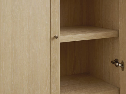 Close-up of Nason Modular Hutch Cabinet in Sand finish. Partially open door, aged nickel knob, interior shelf, visible wood grain.