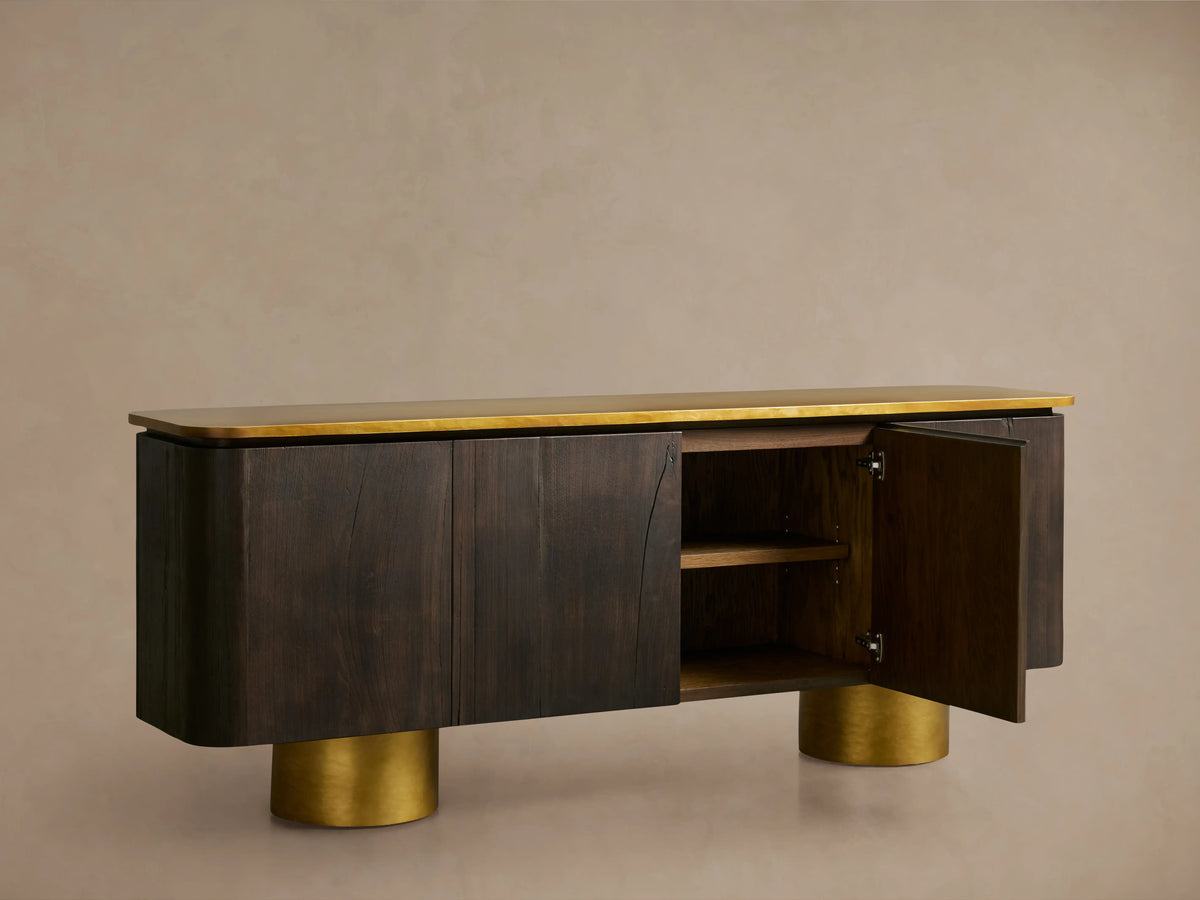 Neira Buffet with dark wood finish and brass top and legs, showing one open door with adjustable shelves inside, against a neutral background.