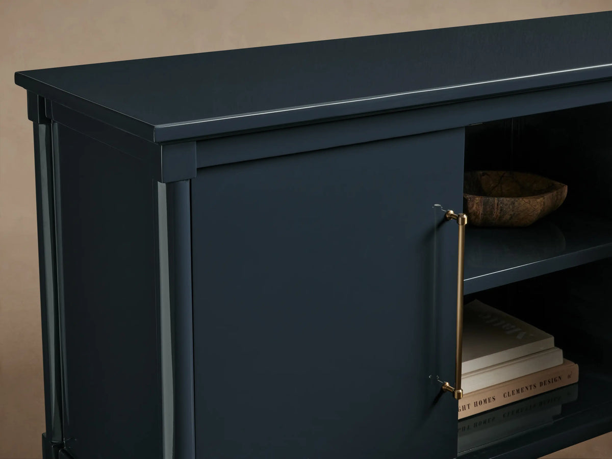 Oakleigh Sideboard in dark blue lacquered finish, features brass hardware, and an open shelf with books and a decorative bowl.
