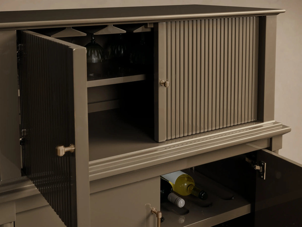 Close-up of the Grey Oakleigh Bar Cabinet. Open reeded doors reveal stemware and wine bottles. Features brass hardware.