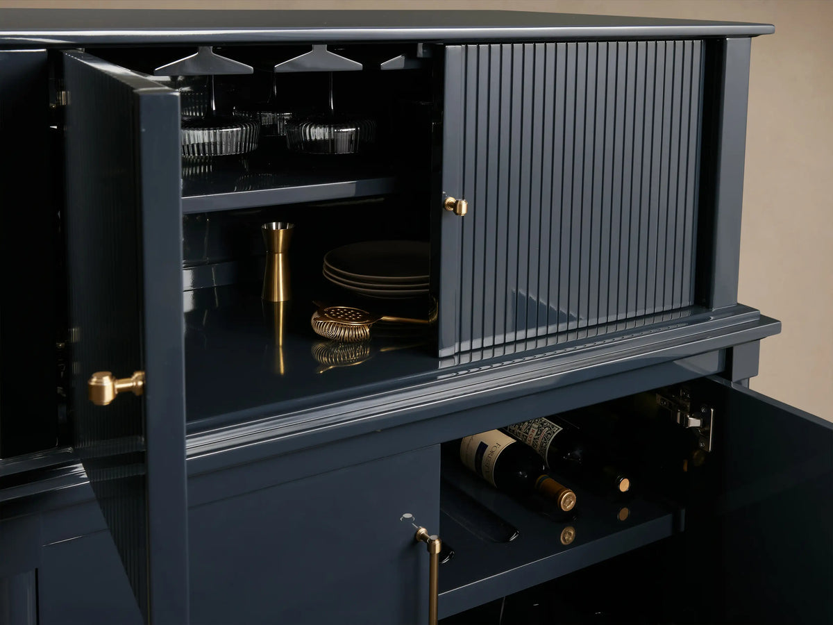 Oakleigh Bar Cabinet in dark finish, featuring open storage with reeded detailing, brass hardware, displaying bottles and stemware.