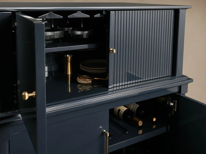 Oakleigh Bar Cabinet in dark finish, featuring open storage with reeded detailing, brass hardware, displaying bottles and stemware.