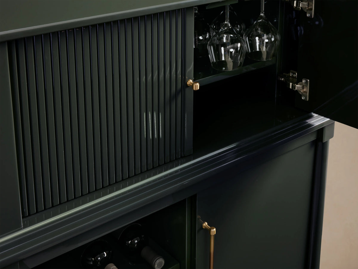 Oakleigh Bar Cabinet in dark green poplar wood with reeded detailing, brass hardware, and dual doors on a wooden floor.