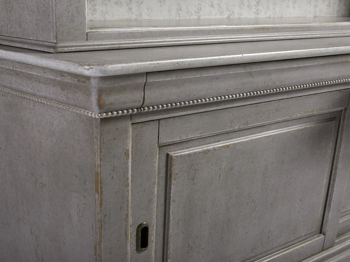 Alt text: Close-up of Giada Bell'Arte Bookcase corner showing hand-applied Antique Grey finish with carved detailing, showcasing its aged look.