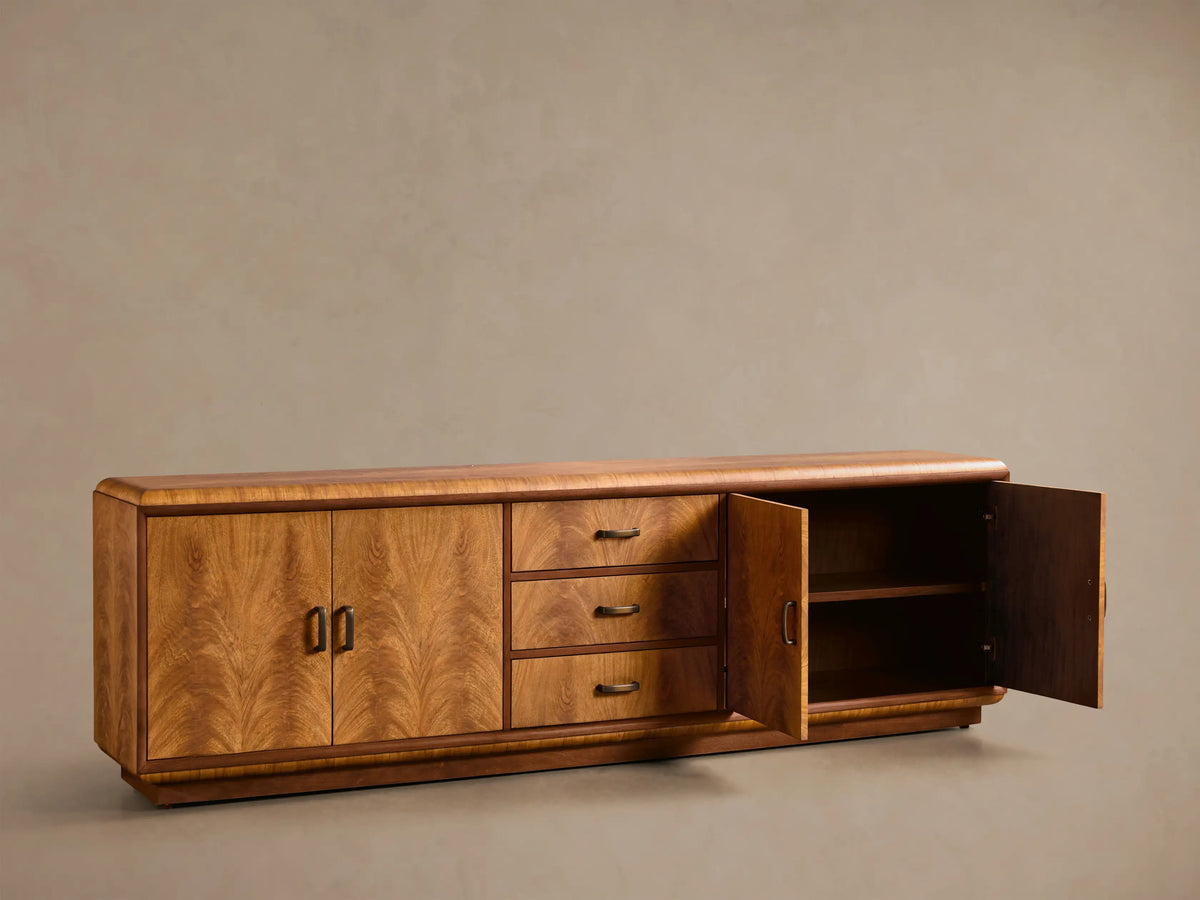 Front view of the Palma Media Console, natural wood veneer with arched graining. Right cabinet open to shelf, three drawers, aged bronze pulls.