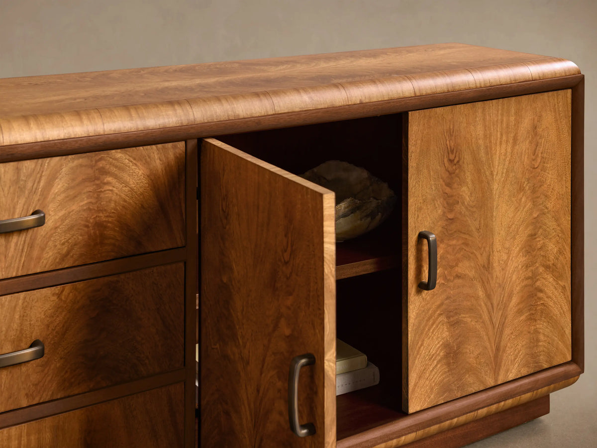 Angled close-up of the brown Palma Media Console. Cerajeira wood veneer, prominent arched graining, three drawers, and open right cabinet with shelf.