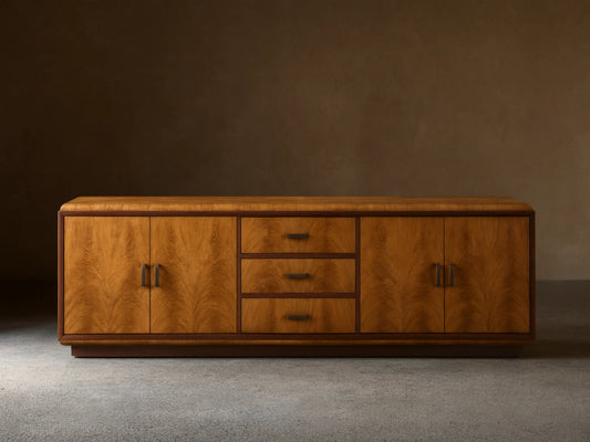 Front view of the Palma Media Console, showing light brown cerajeira wood veneer with cathedral graining, dark trim, and aged bronze hardware.