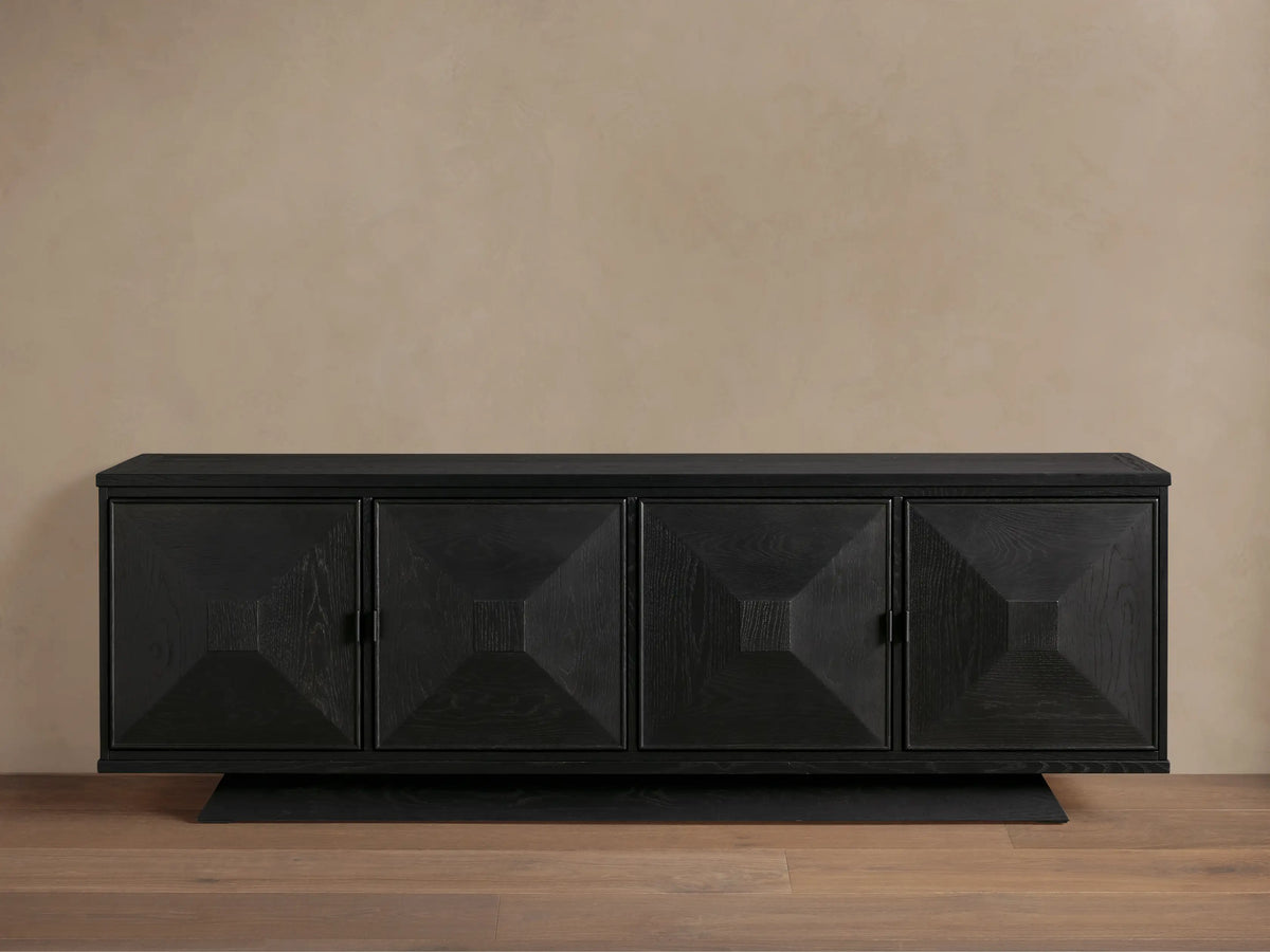 Pelham Sideboard, ebony finish, with four doors featuring recessed square geometric design. Matte black hardware. On a wood floor.