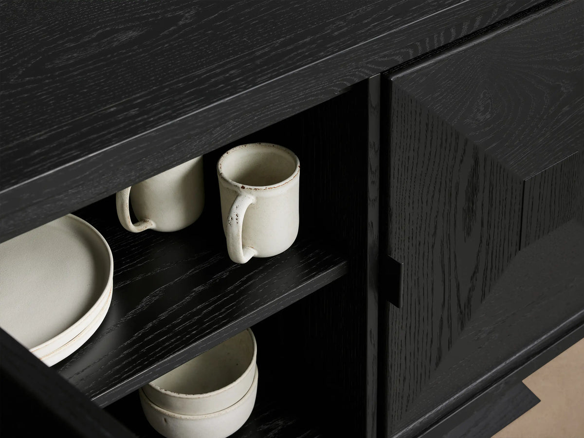 Close-up of open ebony Pelham Sideboard, showcasing visible wood grain, interior shelves with light ceramic mugs, plates, and bowls.