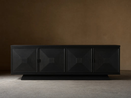 Pelham Sideboard, ebony finish, with four doors featuring recessed square geometric design. Matte black hardware. On a wood floor.