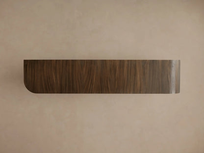 Pliego Sideboard, dark brown guanacaste wood with vertical grain. Rectangular form with a curved left edge, against a light beige wall.