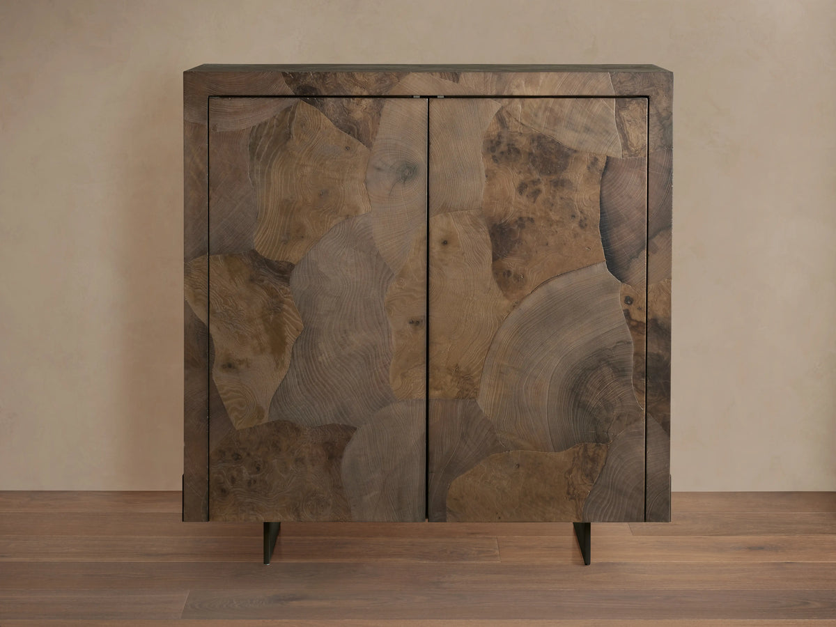 Polanco Bar Cabinet made from oyster-cut ash, showcasing varied textures and tones, with a steel base, set against a wooden floor.