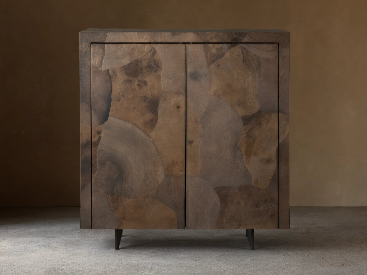 Polanco Bar Cabinet made from oyster-cut ash, showcasing varied textures and tones, with a steel base, set against a wooden floor.
