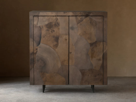 Polanco Bar Cabinet made from oyster-cut ash, showcasing varied textures and tones, with a steel base, set against a wooden floor.