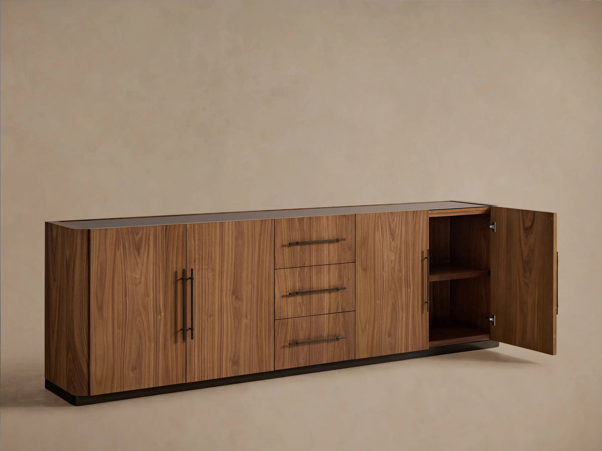 Piermont Sideboard: Long, medium brown walnut wood with smoked glass top, bronze base, 3 drawers, and 2 double-door cabinets.