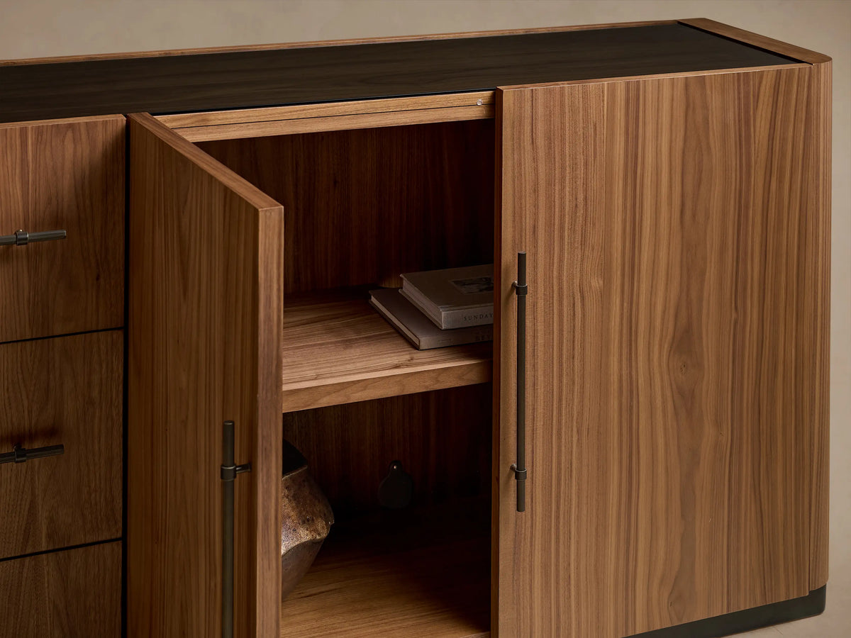 Piermont Sideboard: long walnut wood with smoked glass top and bronze plinth base. Rightmost door open, showing interior shelves.