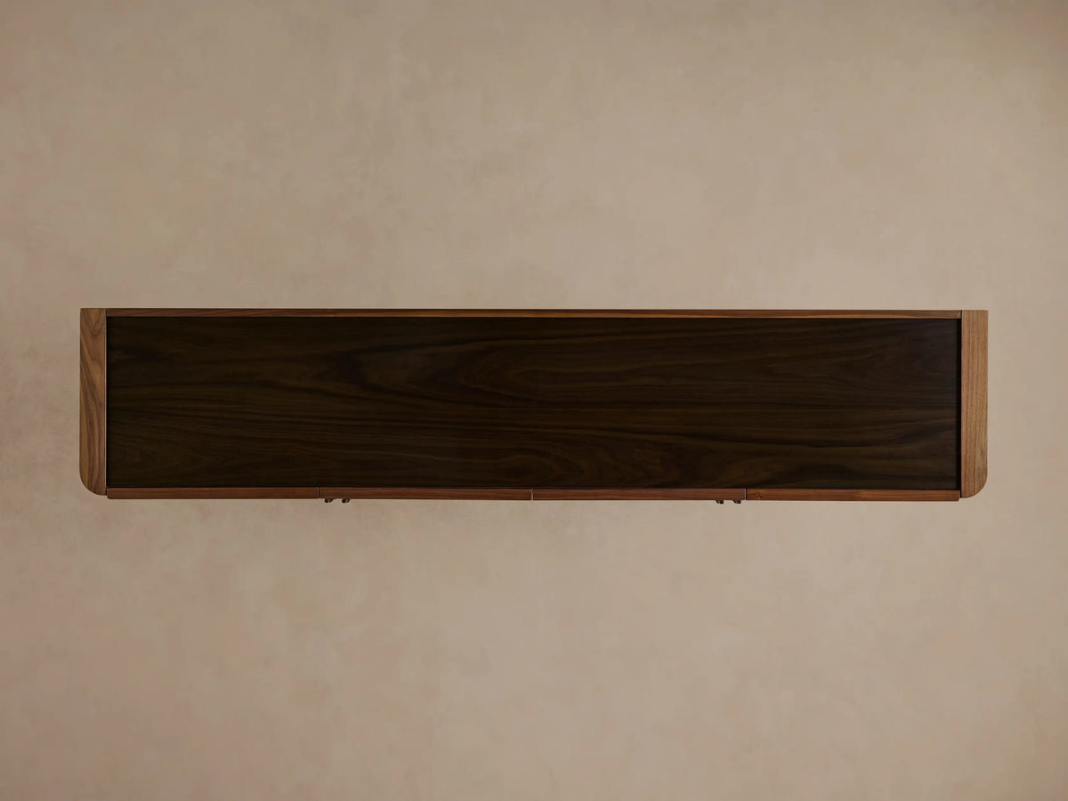 Piermont Sideboard: dark walnut cabinet, one door open revealing internal shelves with vase & book. Smoked glass top, bronze base.