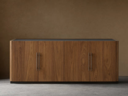 Piermont Sideboard: long walnut wood cabinet with smoked glass top, four doors, bronze handles, and dark bronze plinth base.