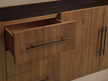 Close-up of Piermont Modular Glass Media Cabinet's dark walnut wood frame & interior shelves behind glass doors with bronze pulls.