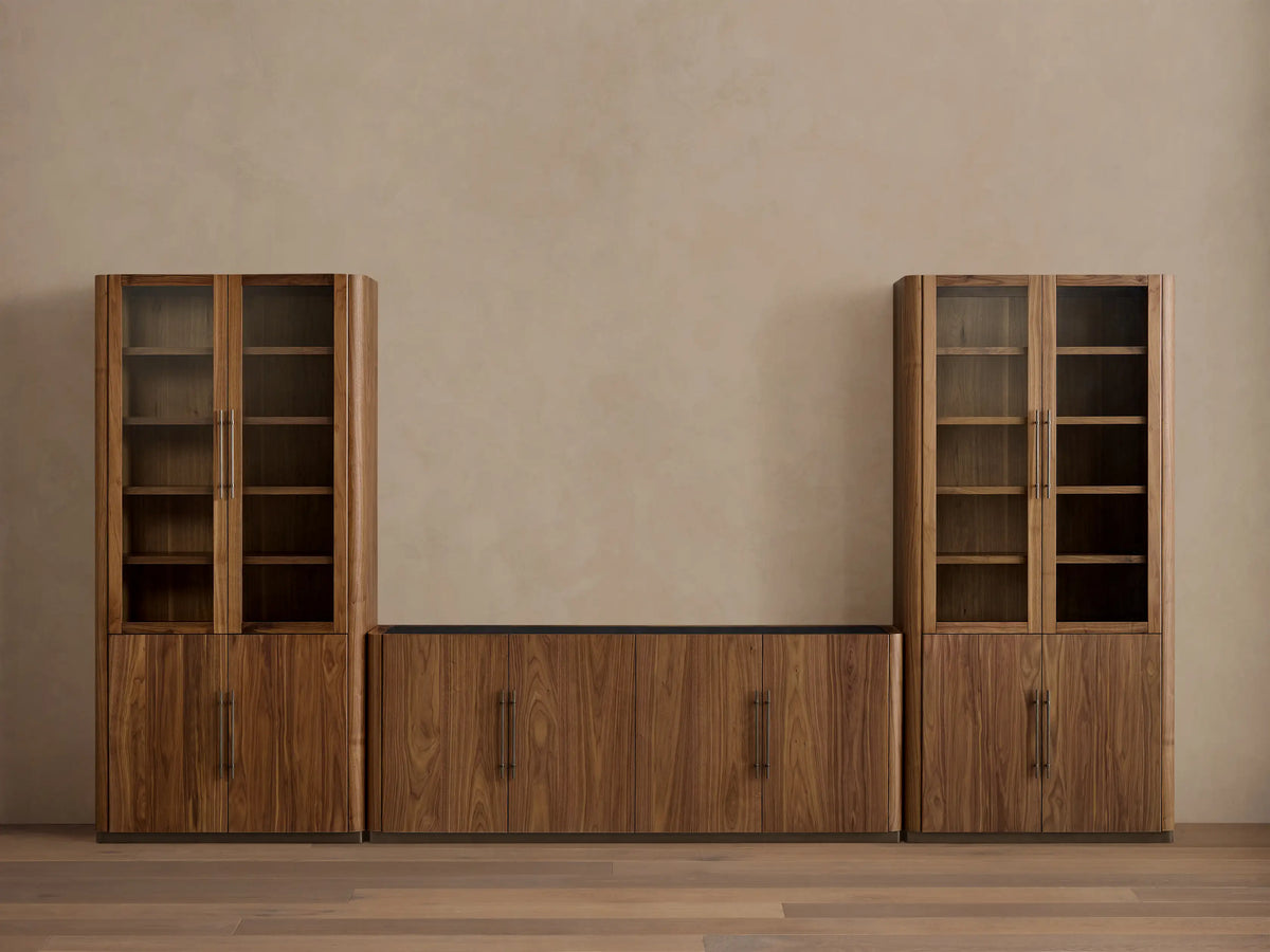 Dark walnut Piermont Modular Media Cabinet Set. Two tall glass-door cabinets flank a low center cabinet under a TV, on bronze bases.