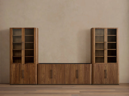 Dark walnut Piermont Modular Media Cabinet Set. Two tall glass-door cabinets flank a low center cabinet under a TV, on bronze bases.