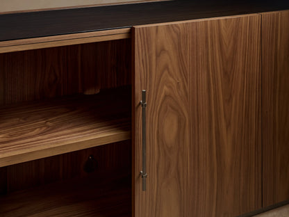 Close-up: Piermont Modular Glass Media Cabinet Set. Dark walnut wood with prominent grain, bronze handles, and plinth base. Glass sections visible.
