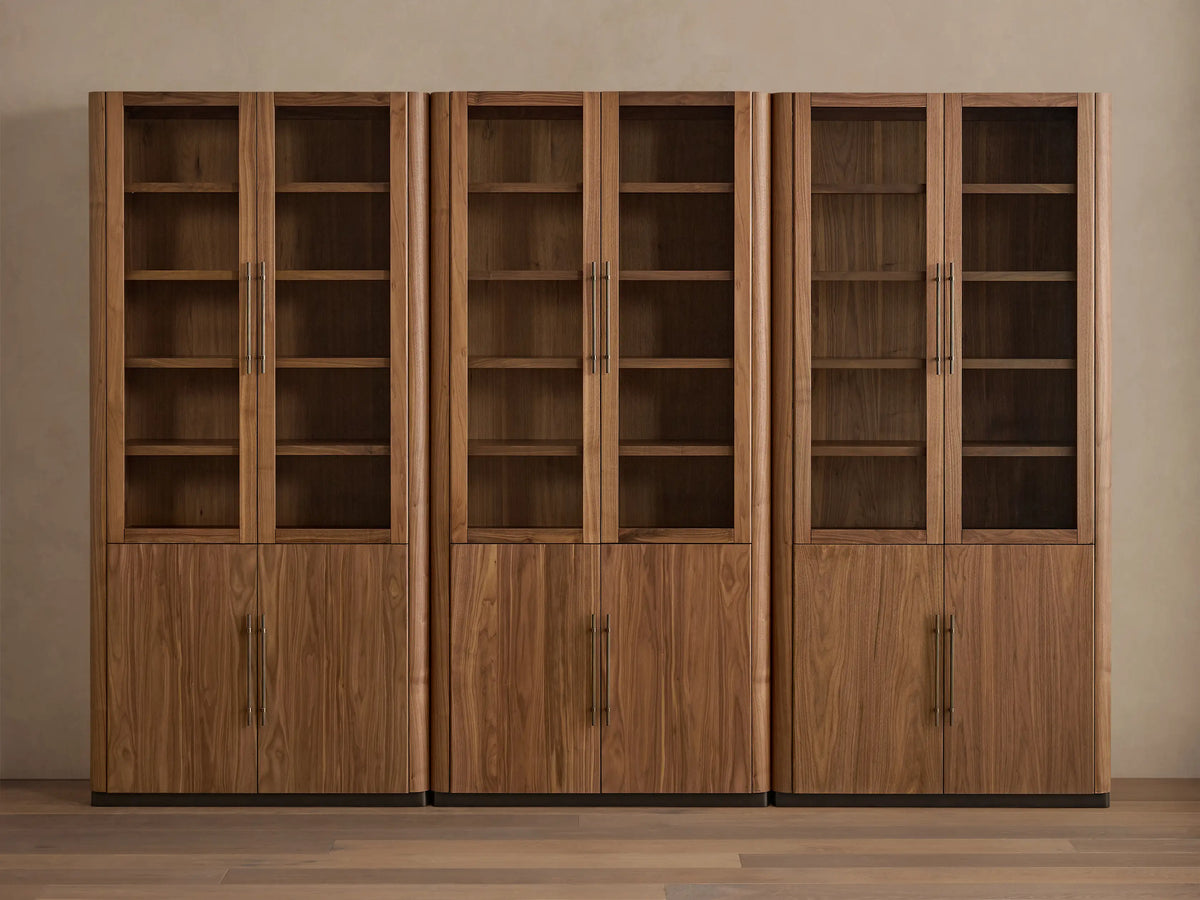 Three Piermont Modular Glass Cabinets made of walnut wood, with glass display doors, brass handles, and dark plinth base, displayed side-by-side.