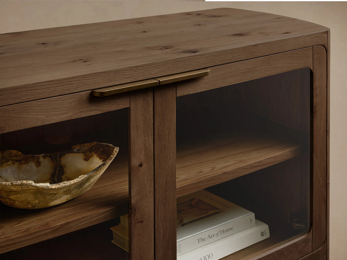 Front view of a rectangular, medium-dark brown oak console with rounded edges. It has four glass-paneled doors, dark handles, and internal wooden shelves.