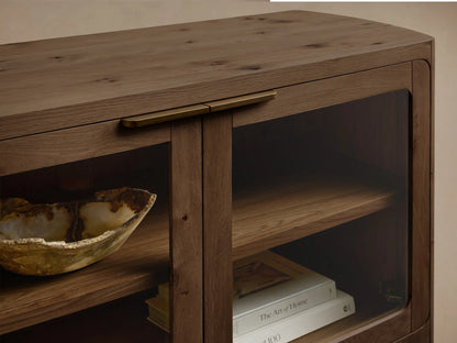 Front view of a rectangular, medium-dark brown oak console with rounded edges. It has four glass-paneled doors, dark handles, and internal wooden shelves.