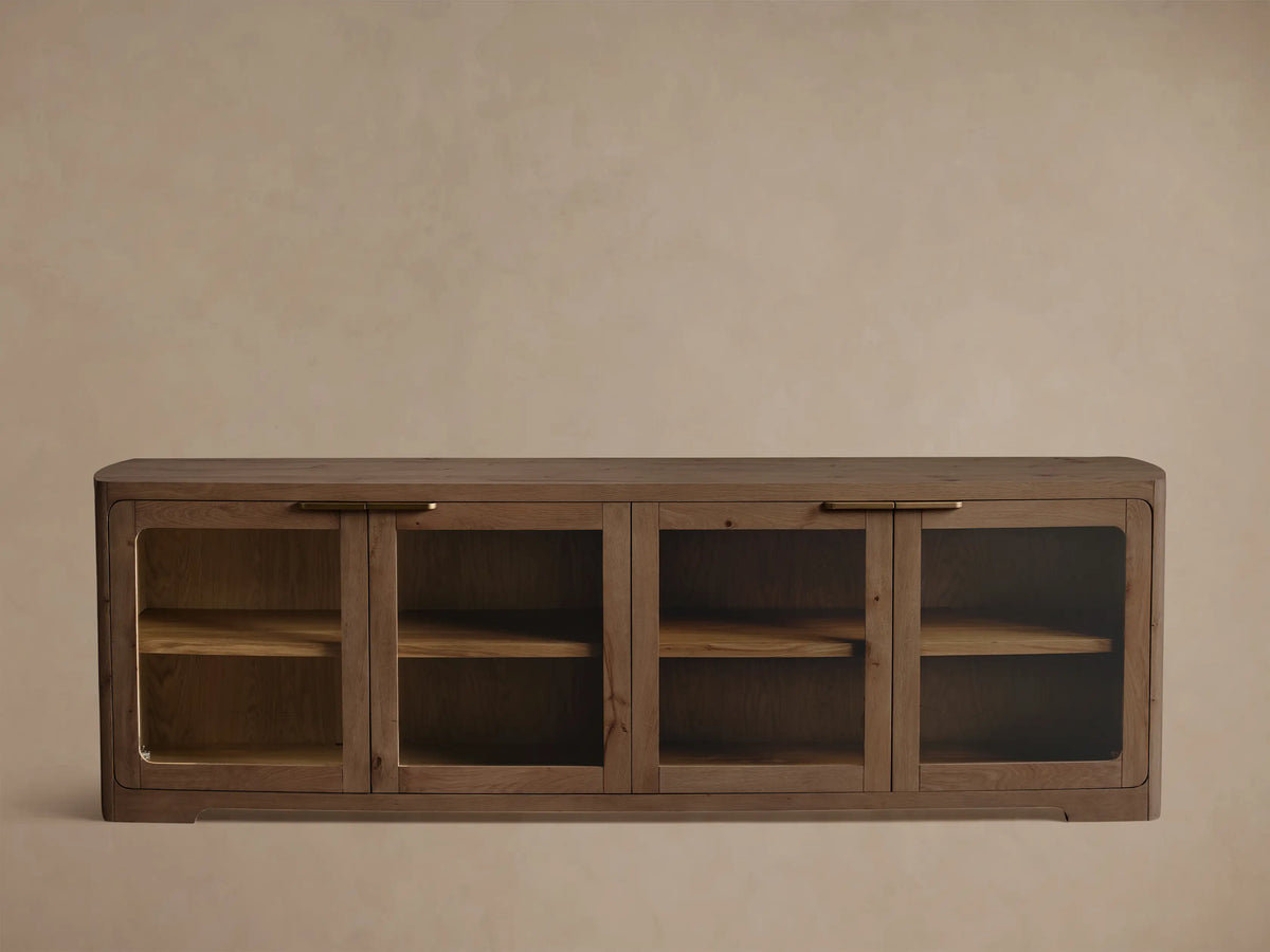 Medium brown oak cabinet with rounded corners, glass doors, brass handle, and shelves displaying a bowl and books.