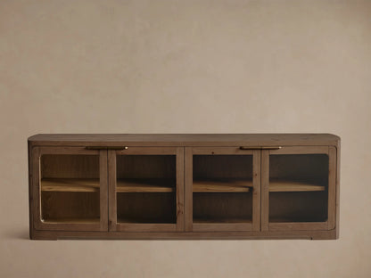 Medium brown oak cabinet with rounded corners, glass doors, brass handle, and shelves displaying a bowl and books.