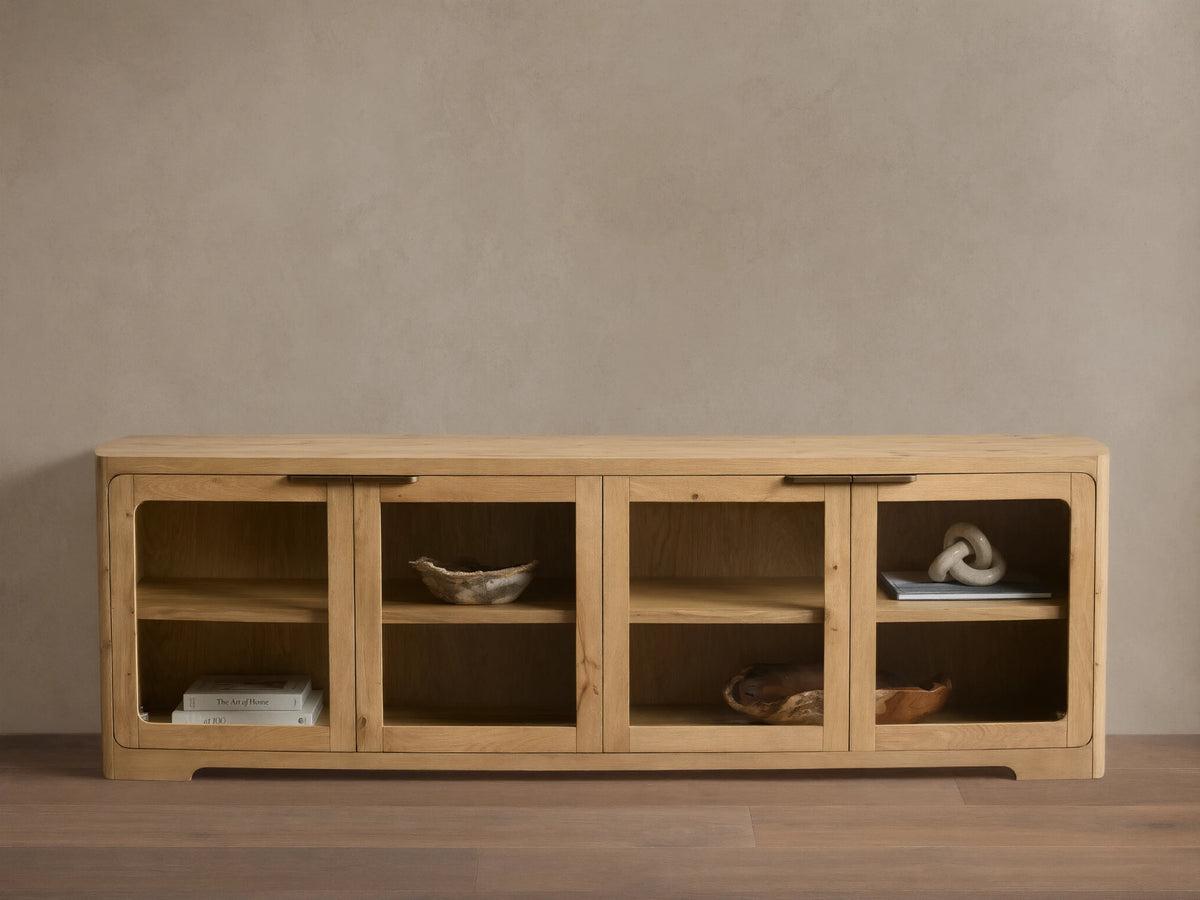 Front view of a light natural wood cabinet with four glass doors, rounded corners, interior shelves, and dark metal handles.