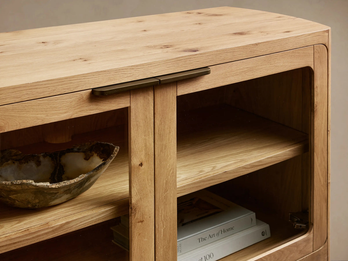 Front view of light natural wood cabinet with four glass doors, dark handles, and interior shelves.