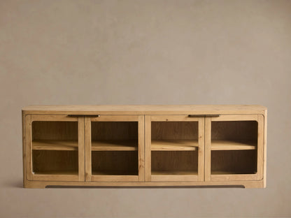 Close-up of light oak wood cabinet with visible grain, rounded top, glass doors, and brass bar handle.