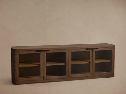 Front view of a dark wood console with rounded edges, four clear glass doors, brass-colored handles, and internal shelves.