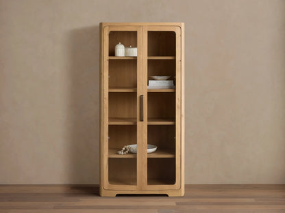 Front view of natural wood Redding Glass Cabinet with two glass doors, four shelves, and antique brass hardware.