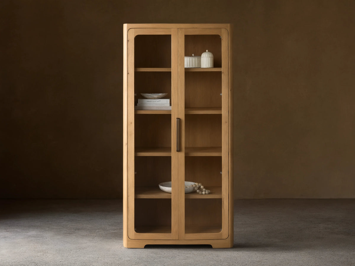 Front view of natural wood Redding Glass Cabinet with two glass doors, four shelves, and antique brass hardware.