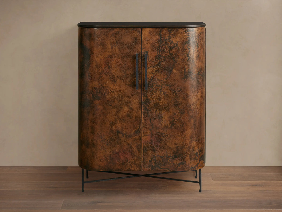 Ruiz Bar Cabinet: Curved, two-door cabinet with fiery orange-brown hand-hammered copper doors, black handles, dark top, and iron base.