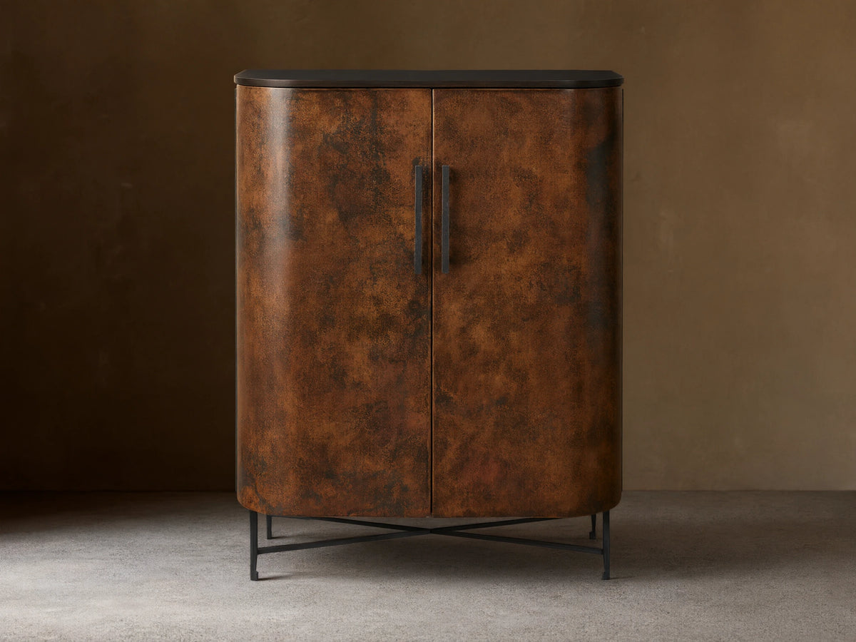 Ruiz Bar Cabinet: Curved, two-door cabinet with fiery orange-brown hand-hammered copper doors, black handles, dark top, and iron base.