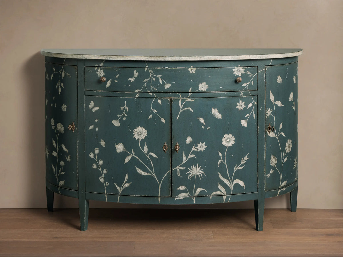 Front view of the distressed dark teal Sofia Bell'Arte Demilune Cabinet with white hand-painted floral and butterfly motifs and light top.