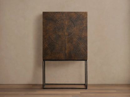 Theota Bar Cabinet with a dark brown sunburst pattern on teak, resting on slender black metal legs against a beige wall.