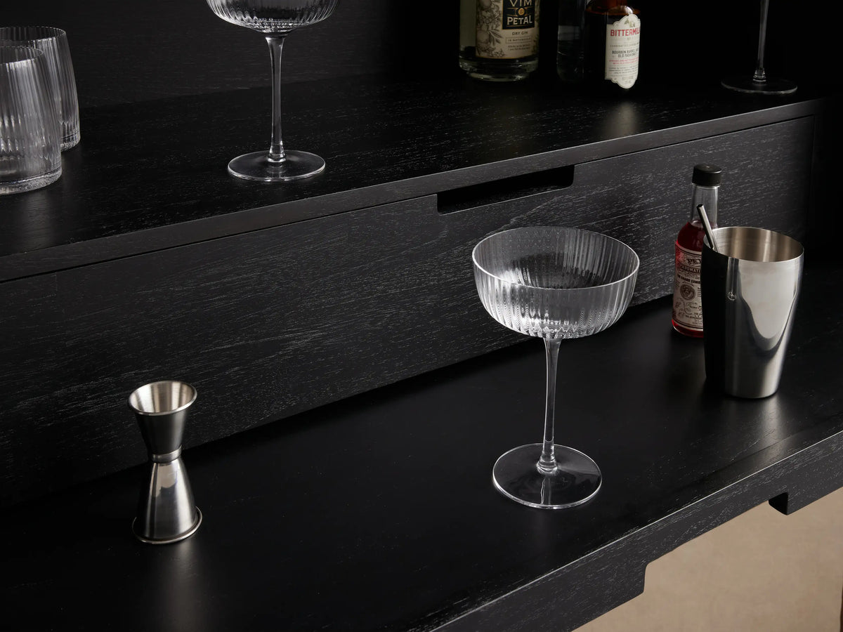 Theota Bar Cabinet with sunburst pattern on teak wood, showing hand-stamped texture, partial view of interior with glassware.