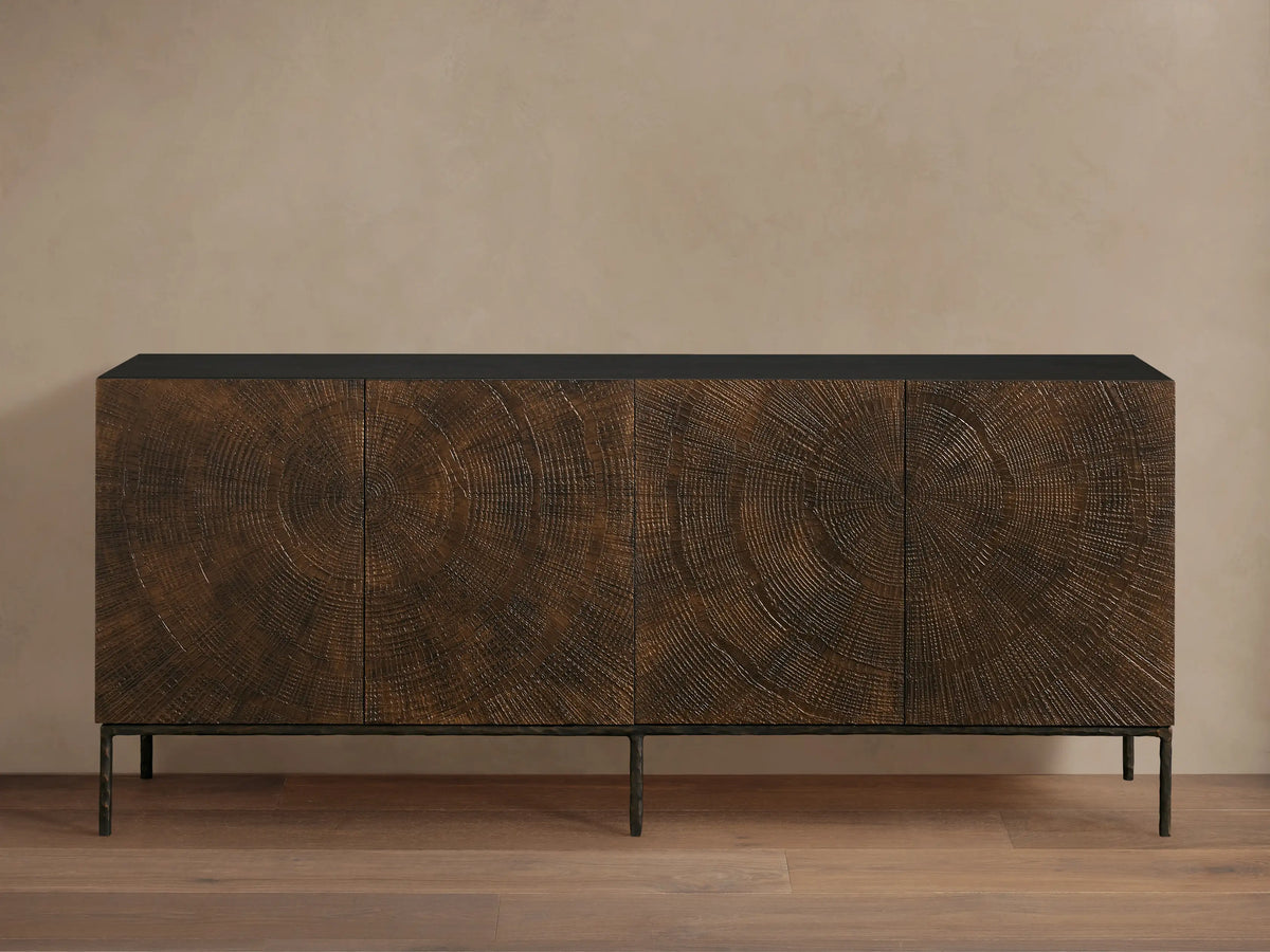 Theota Sideboard: dark brown teak wood with hand-stamped sunburst pattern across its 4 doors, black top, dark hammered aluminum legs.