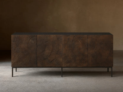 Theota Sideboard: dark brown teak wood with hand-stamped sunburst pattern across its 4 doors, black top, dark hammered aluminum legs.