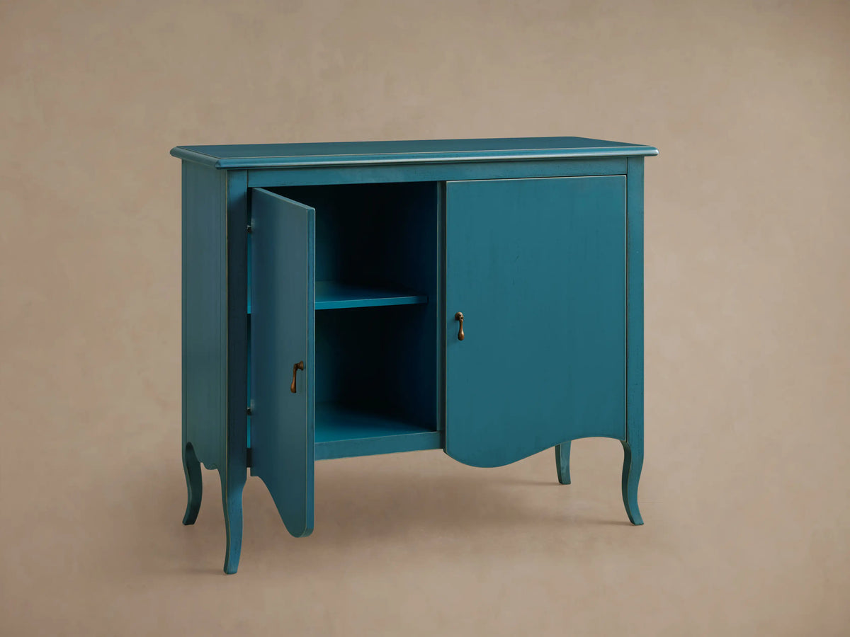 Varzi Cabinet in teal blue with antique pendant pull hardware, open left door revealing two shelves, curved legs.